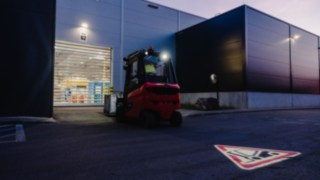 Ein Linde-Stapler, ausgerüstet mit dem Linde TruckSpot, fährt bei Dämmerung rückwärts aus der Halle. Ein Linde-Stapler, ausgerüstet mit dem Linde TruckSpot, fährt bei Dämmerung rückwärts aus der Halle.
